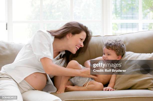 pregnant mother and son playing on sofa - tickling stock-fotos und bilder