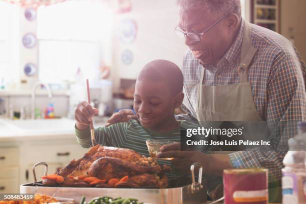 older man and grandson cooking together in kitchen - basted stock pictures, royalty-free photos & images