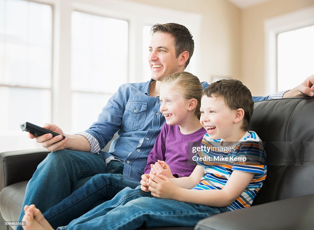 Caucasian father and children watching television on sofa