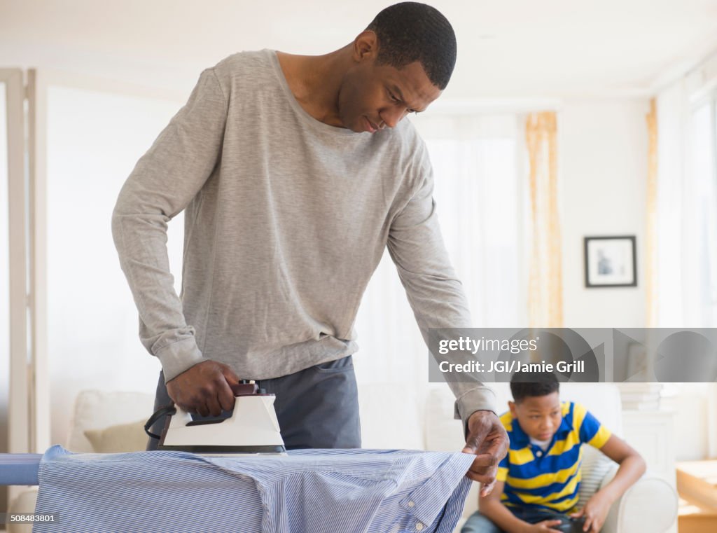 Father ironing shirt while son plays video games