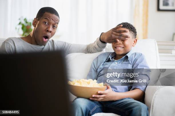 father and son watching television on sofa - bad news on tv stock pictures, royalty-free photos & images