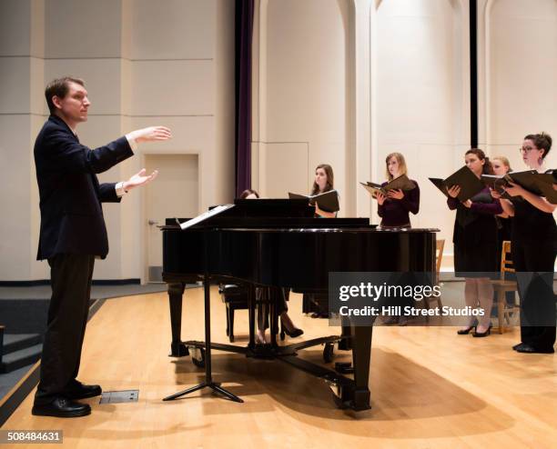 conductor directing choir on stage - dirigent stock-fotos und bilder