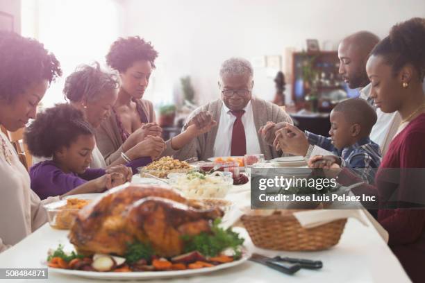 family saying grace at holiday table - black people praying stock pictures, royalty-free photos & images