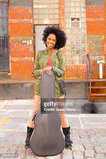 mixed race woman with guitar case on city street - afro caribbean and american stock-fotos und bilder