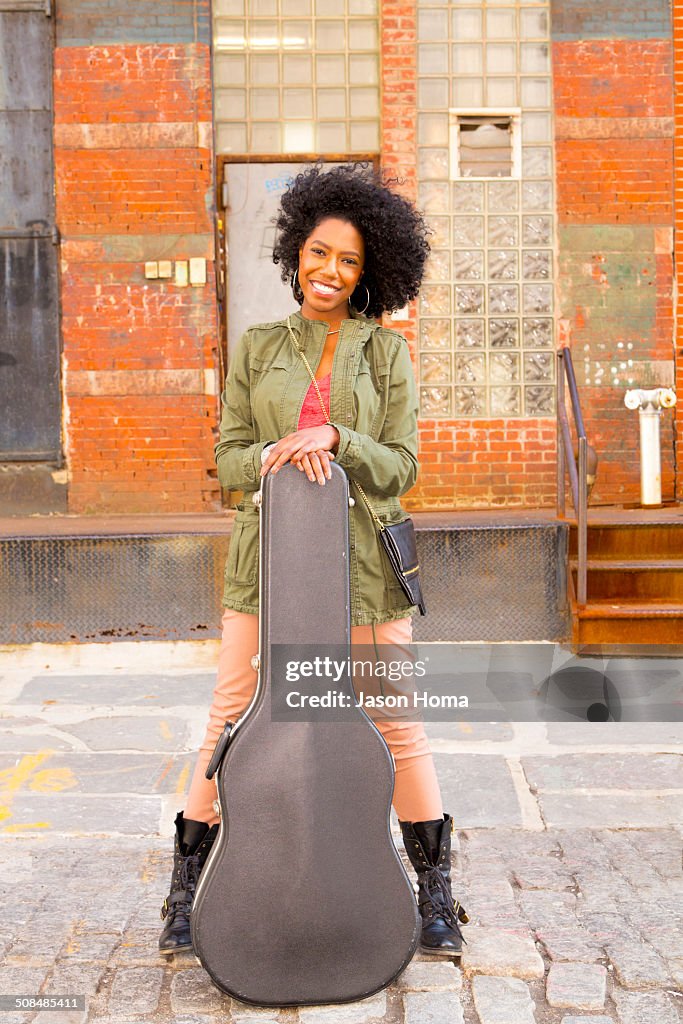 Mixed race woman with guitar case on city street