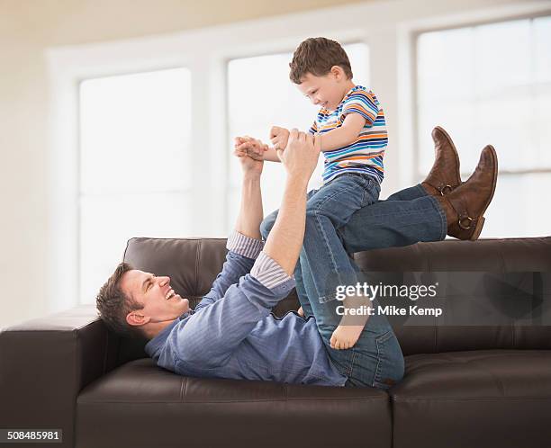 caucasian father and son playing on sofa - knees together - fotografias e filmes do acervo