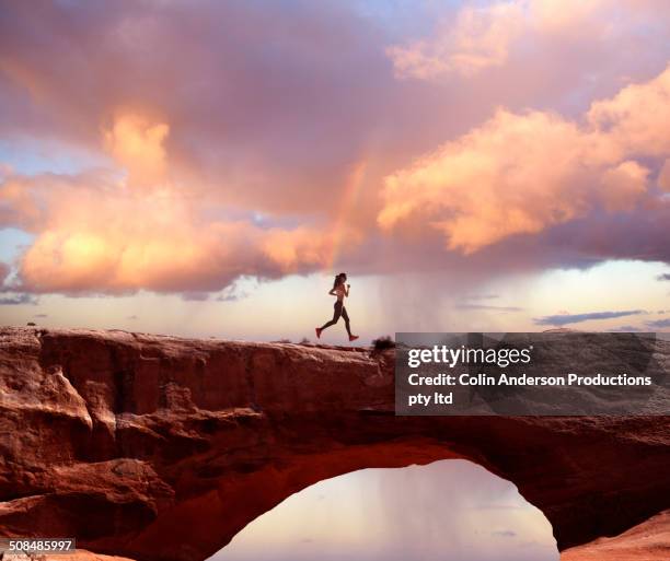 pacific islander woman jogging on rock arch - läufer dramatisch stock-fotos und bilder