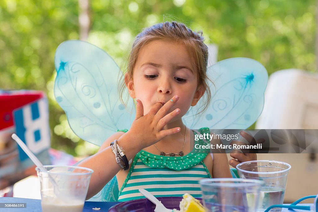 Caucasian girl eating cake at birthday party