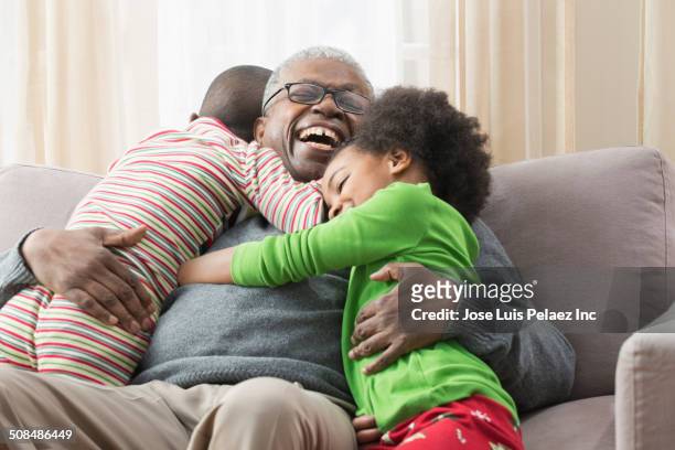 older man hugging grandchildren on sofa - grandfather stock pictures, royalty-free photos & images