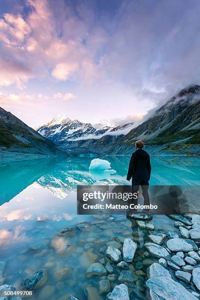landscape: hiker looking at mt cook from lake with iceberg, new zealand - mt cook stock-fotos und bilder