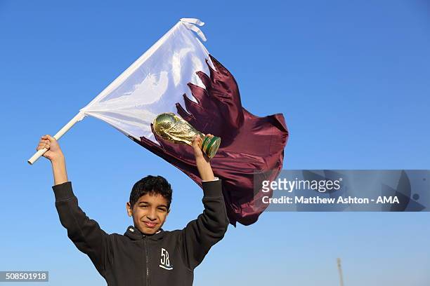 Football fan holding the maroon and white national flag of Qatar with a replica of the FIFA World Cup Trophy in Doha, Qatar, the host venue for the...