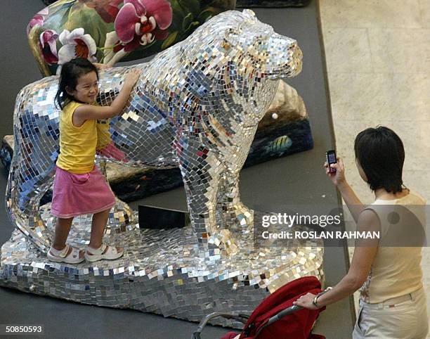 Woman takes a photograph of her daughter with a mobile phone next to a unique series of lion sculptures displayed in a shopping mall, in Singapore 18...