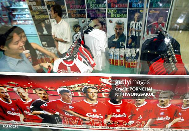 Thai couple chooses a jersey next to a promotional poster showing players from England's Premier League football club Liverpool at a football...