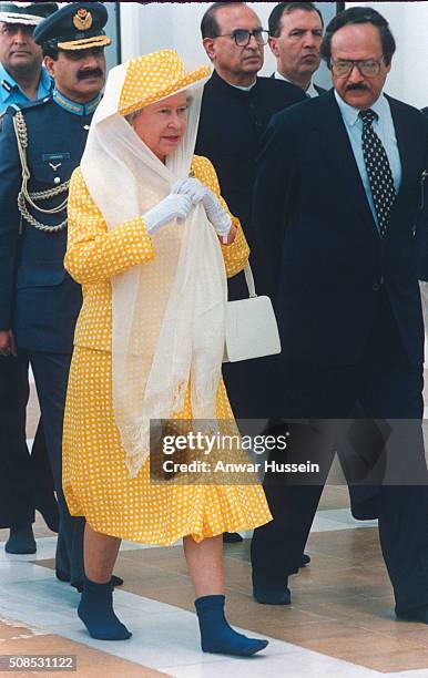 Queen Elizabeth II, wears a scarf over her hat to cover her hair and walks in socks without shoes as a sign of respect as she visits the Shah Faisal...