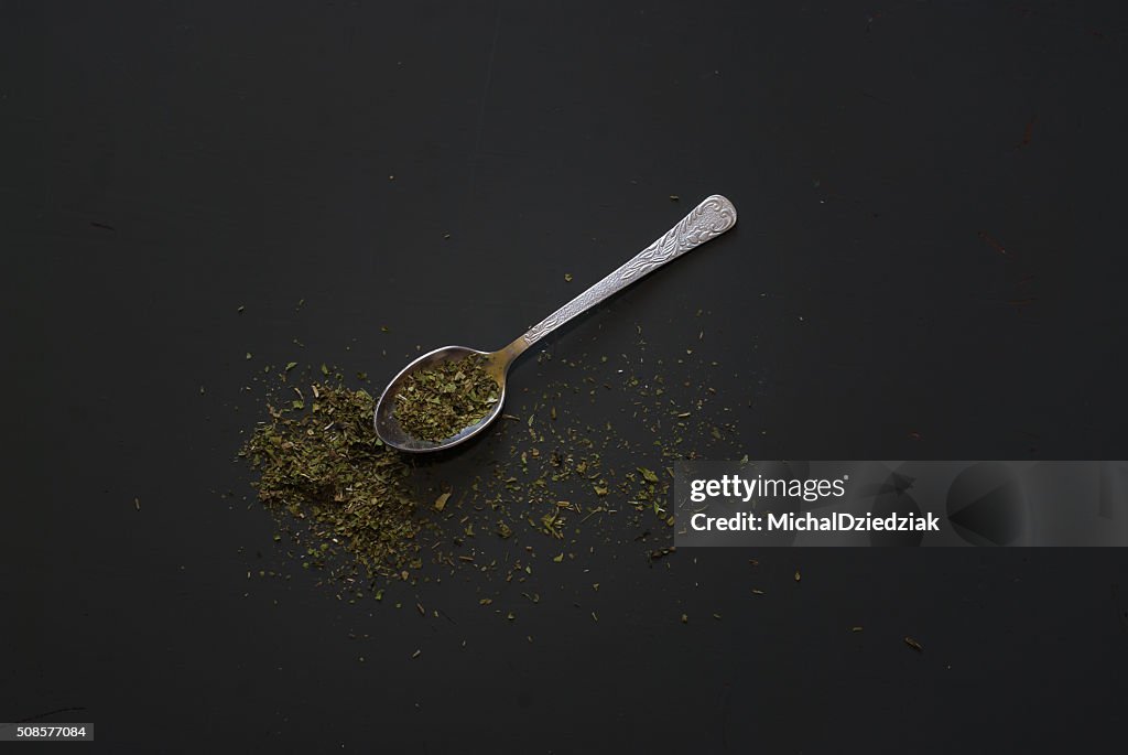 Dried basil on metal teaspoon on dark wooden table