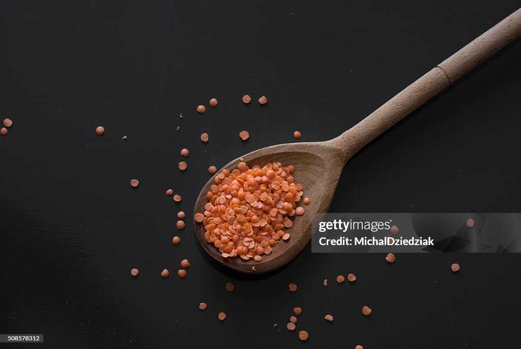 Red lentil on wooden spoon on dark wooden table