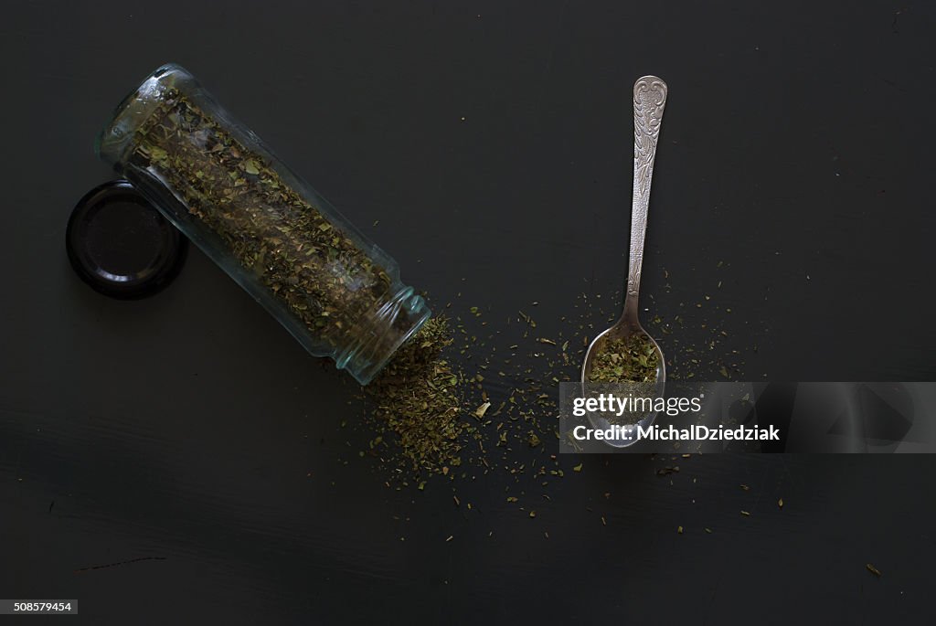 Dried basil on metal teaspoon on dark wooden table