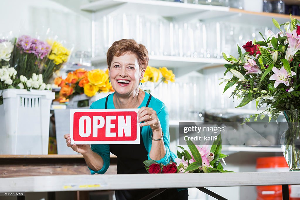 Mature woman in flower shop holding OPEN sign