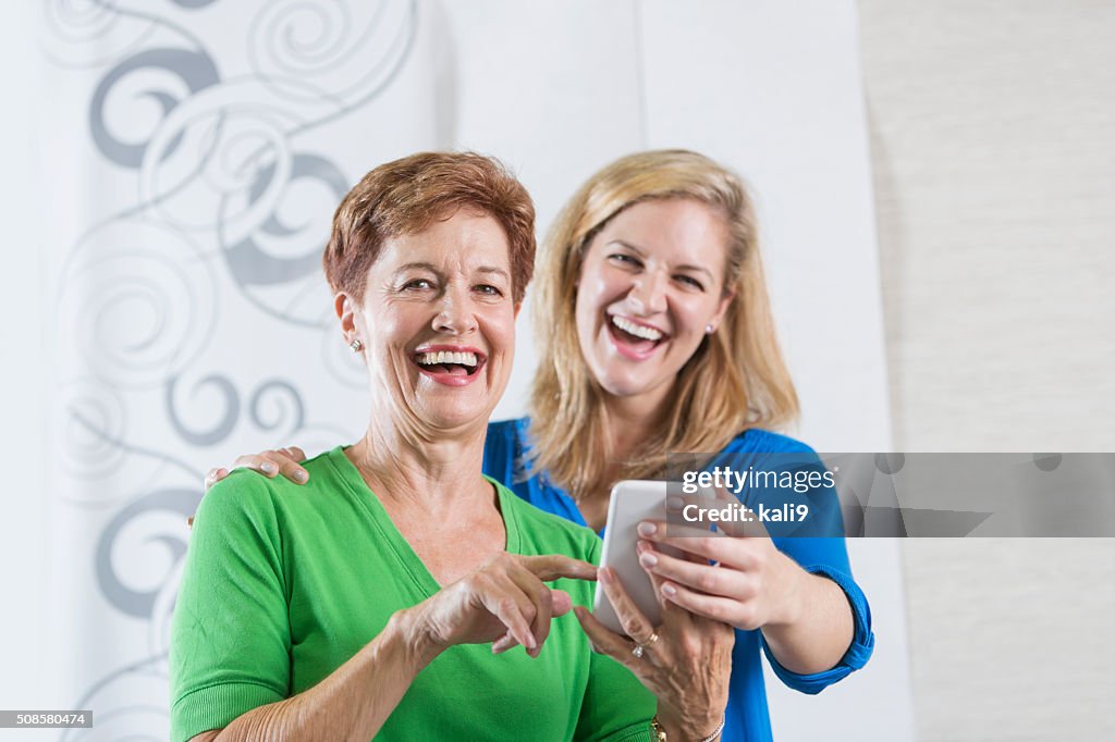 Senior woman and adult daughter laughing at phone