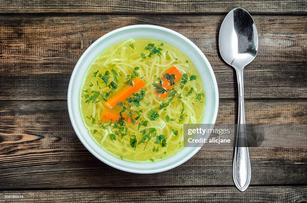 Chicken broth soup with noodles on a wooden table.