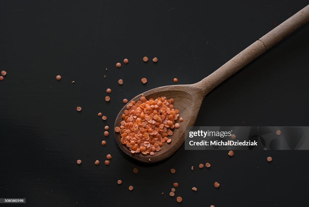 Red lentil on wooden spoon on dark wooden table