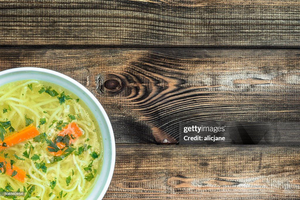 Chicken broth soup with noodles on a wooden table.