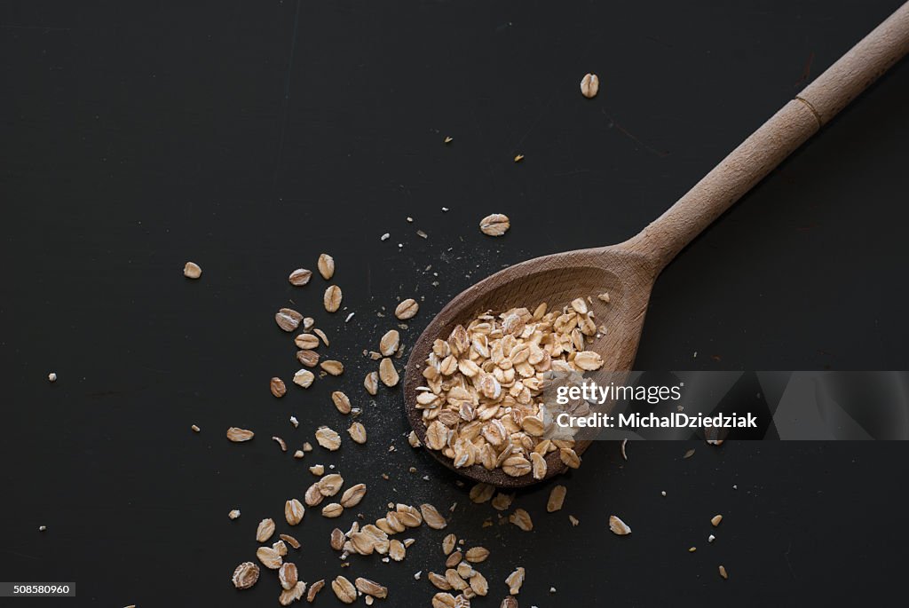 Oat flakes on wooden spoon on dark wooden table