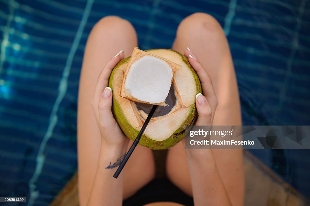 Frau hält Kokosnuss im Swimmingpool