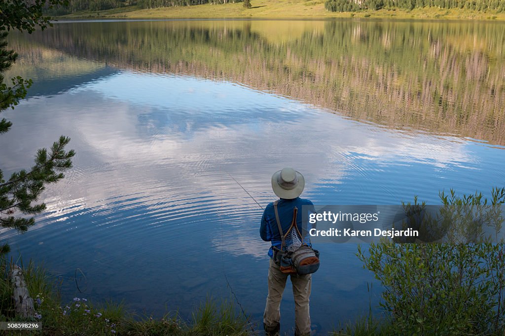 Fly fisherman at mountain lake with reflections