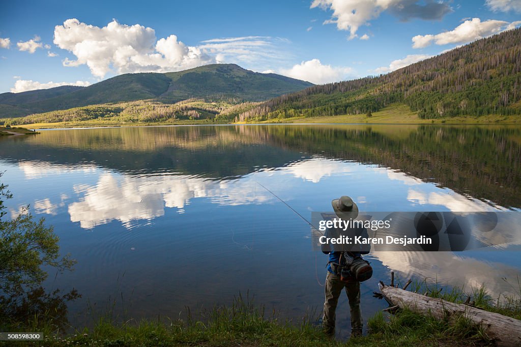 Fly fisherman at mountain lake with reflections