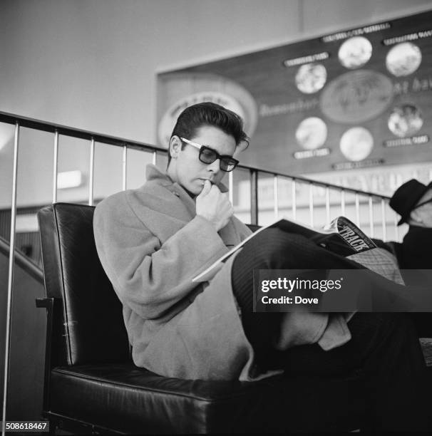 English pop singer, musician, performer, and actor, Cliff Richard reads a magazine whilst waiting at the airport, 12th December 1964.