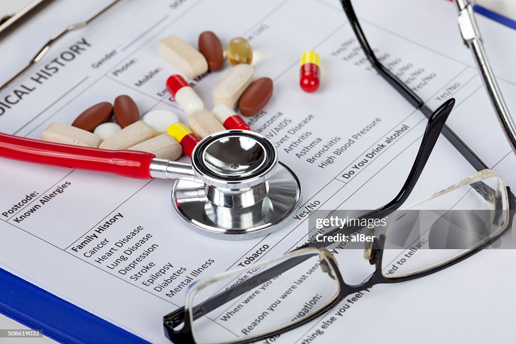 Stethoscope with eyeglasses and pills laying in a medical form