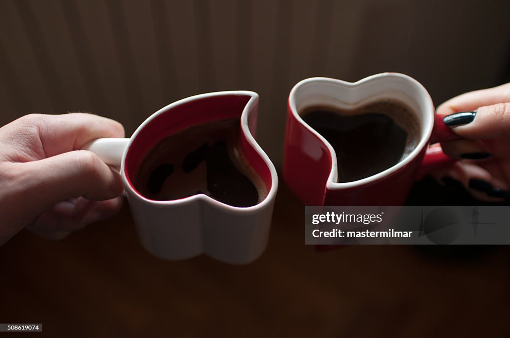 Man and woman holding heart shaped cups with coffee