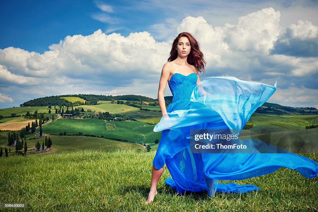 Women wearing blue long dress at sunset in Tuscany field.