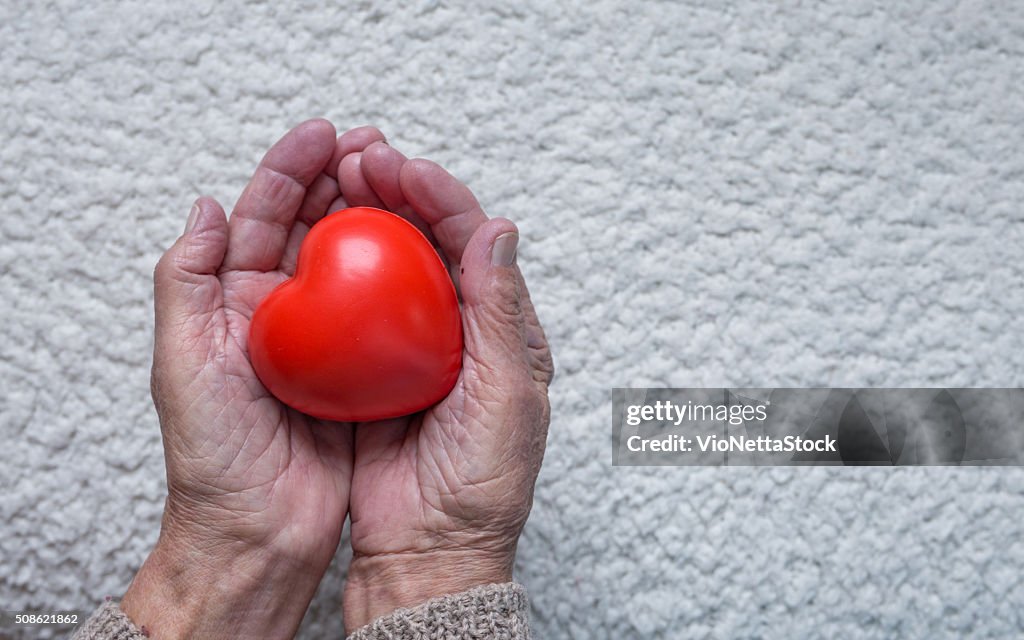 Old woman hands holding red heart, top view