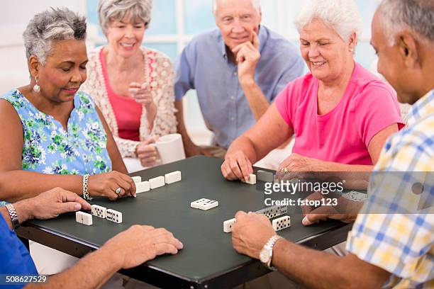 senior adult friends playing dominoes. home or community center setting. - nursing home interior stock pictures, royalty-free photos & images