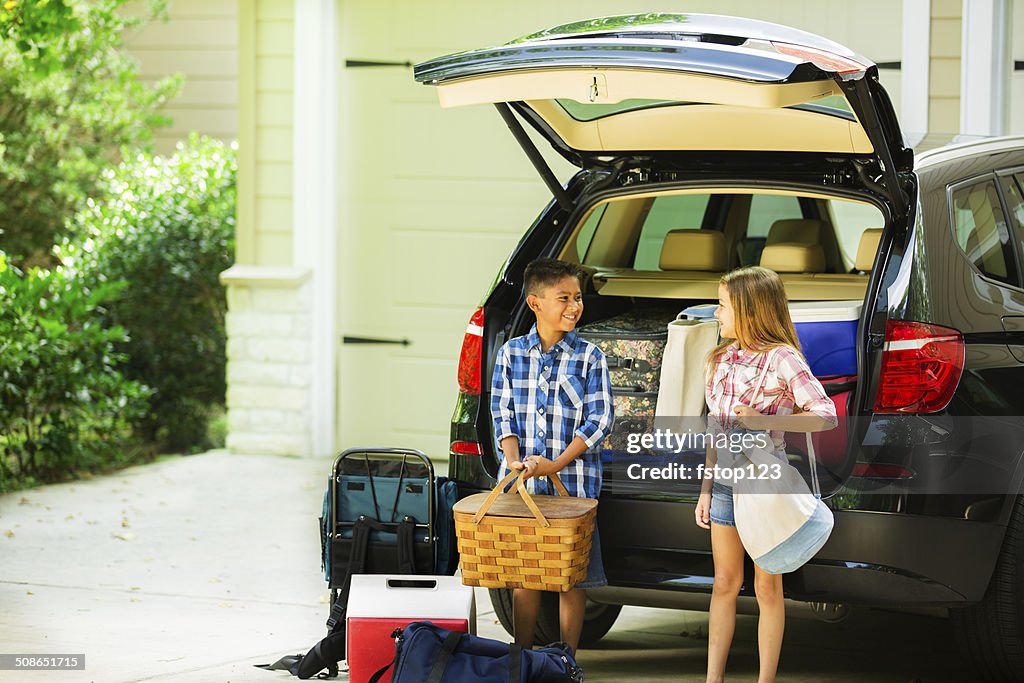 Brother, sister packing car to go on summer family vacation.
