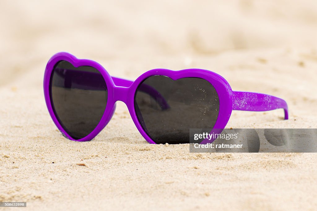Viola occhiali da sole di forma cuore sulla sabbia