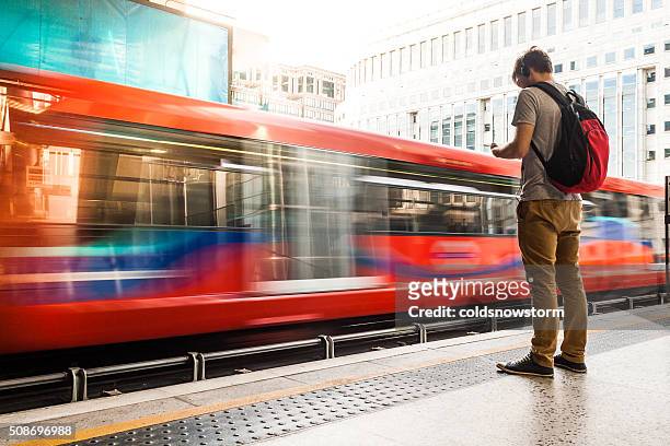 young man with backpack and headphones waiting for train - london england stockfoto's en -beelden