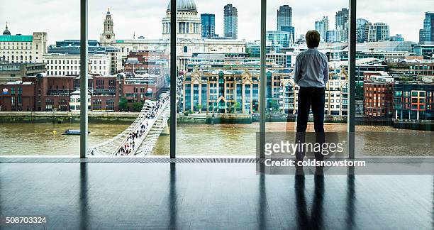 businessman looks at the london skyline from his office window - capitalism stock pictures, royalty-free photos & images