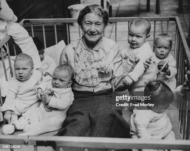 Agnes Baden-Powell, sister of Girl Guide leader Lady Olave Baden-Powell, pictured sitting in a play pen with a group of babies at Westminster Day...