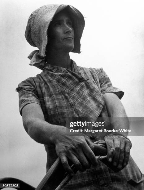 Portait of woman sharecropper wearing a bonnet w. Her hand on the handle of a plow.