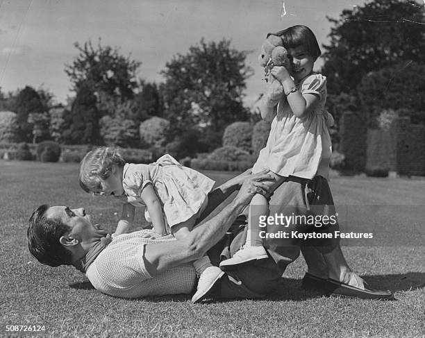 Portrait of actor Tyrone Power playing on the grass with his young daughters Romina and Taryn, circa 1955.