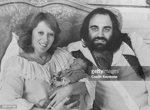 Portrait of Greek singer Demis Roussos sitting on a bed with wife and newborn baby, September 18th 1975.