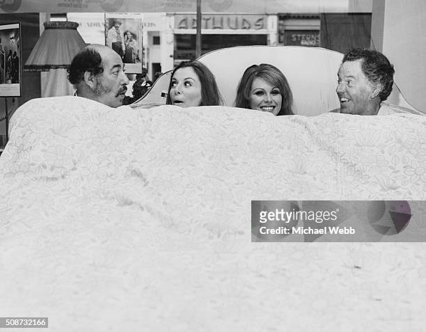 Actors Alfred Marks, Deborah Grant, Joanna Lumley and Brian Rix lying in bed together in the window of Maples department store, promoting their West...