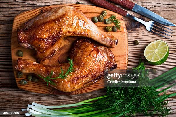two grilled chicken legs, green onion, dill and lime on wooden board viewed from above - hühnchenunterschenkel stock-fotos und bilder