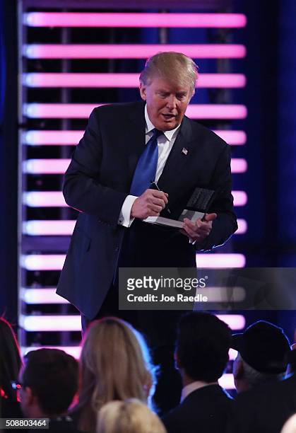 Republican presidential candidate Donald Trump autographs a book during a commercial break in the Republican presidential debate at St. Anselm...