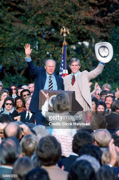 Standign next to his son, American President Gerald Ford waves to a crowd of supporter from behind a podium during his re-election campaign, October...