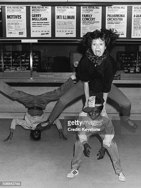 English actress Julie Walters playing leapfrog with two young breakdancers at the Royal Festival Hall, London, January 1985.
