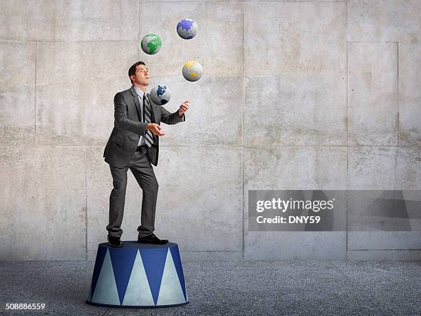 businessman standing on pedestal juggling various globes of earth - juggling stock pictures, royalty-free photos & images